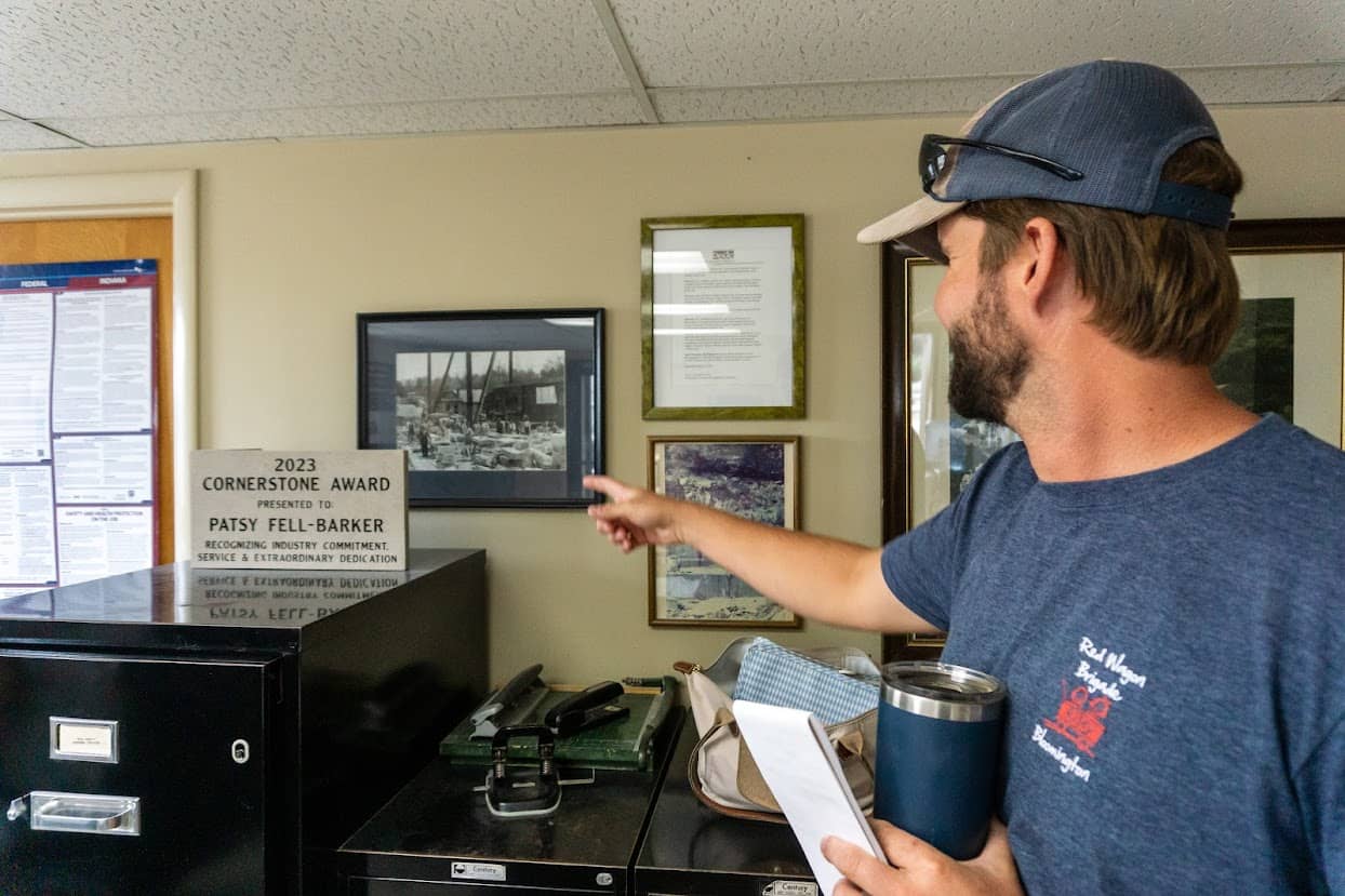 Garrett Fell, President of B.G. Hoadley Quarries Inc., pointing at a framed historical photo next to a 2023 Cornerstone Award plaque honoring Patsy Fell-Barker.