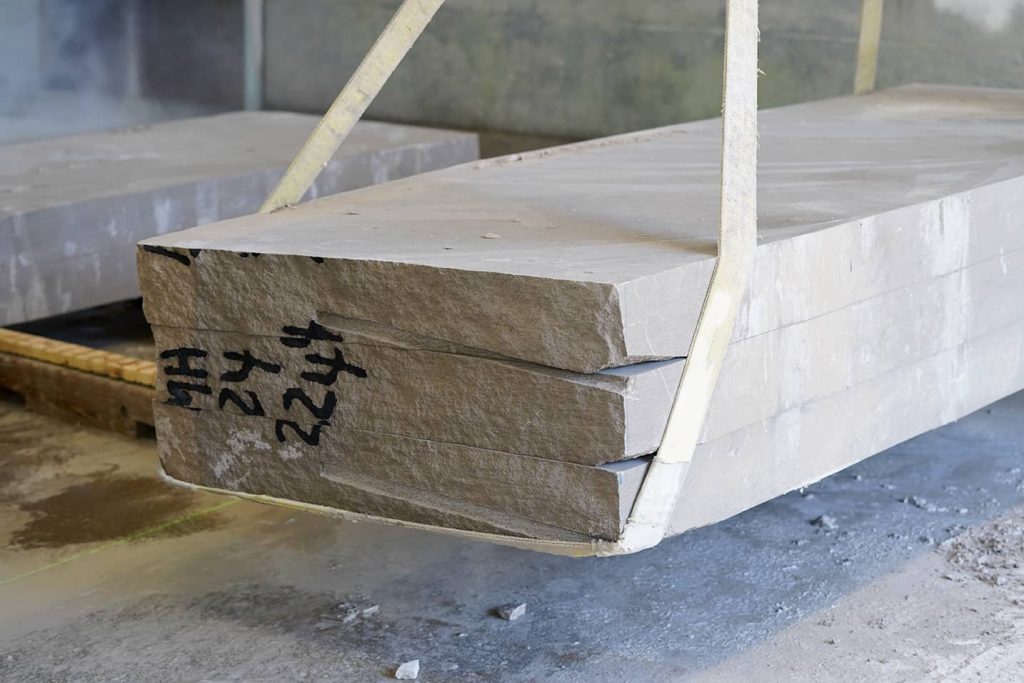 Large slabs of Indiana limestone with rough edges suspended by lifting straps at a stone fabrication facility
