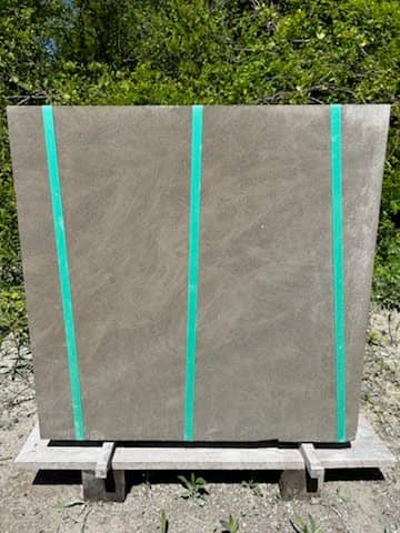 A large concrete paver with three turquoise vertical straps, standing upright on a wooden pallet in an outdoor setting.