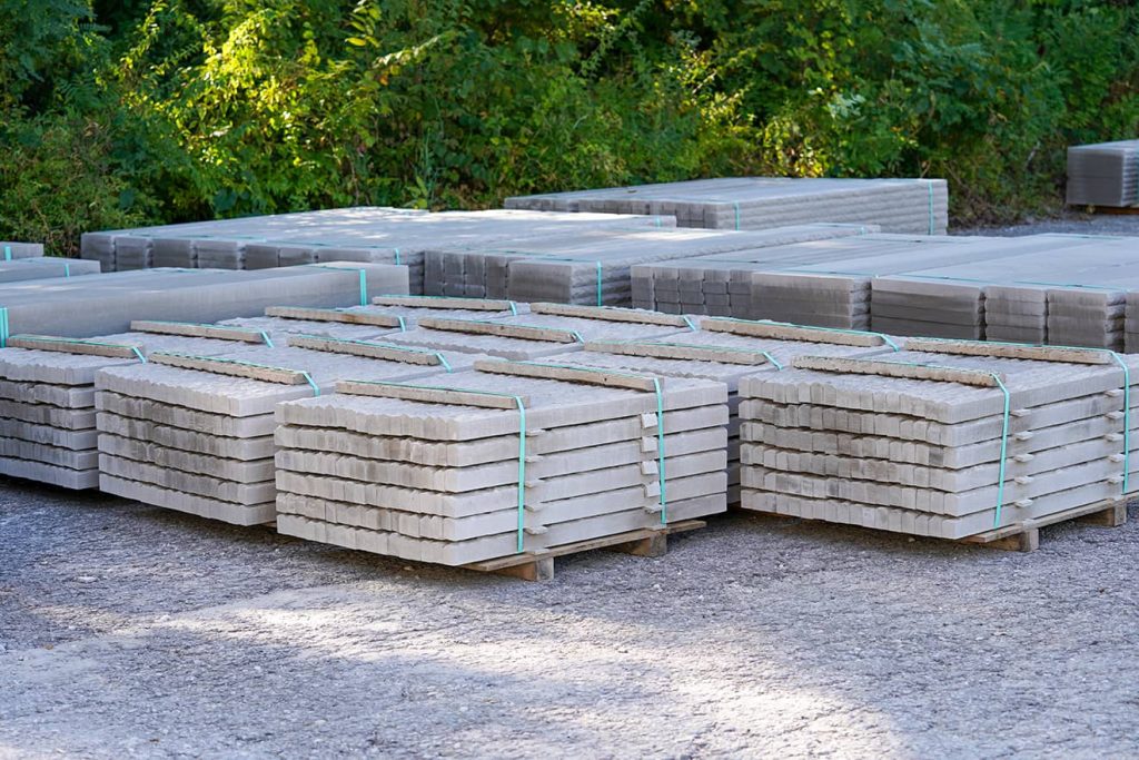 Stacks of rectangular limestone blocks strapped on pallets, stored outdoors for use in paving and retaining wall projects