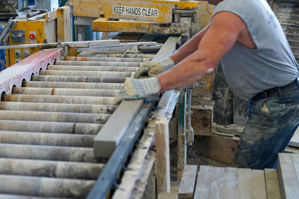 Worker operating a precision stone cutting machine to shape limestone blocks at a mill, wearing gloves for safety