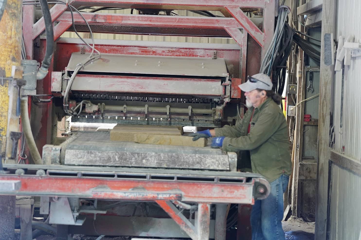 Worker operating a stone slab processing machine in an industrial setting, positioning a sandstone block on a conveyor system.