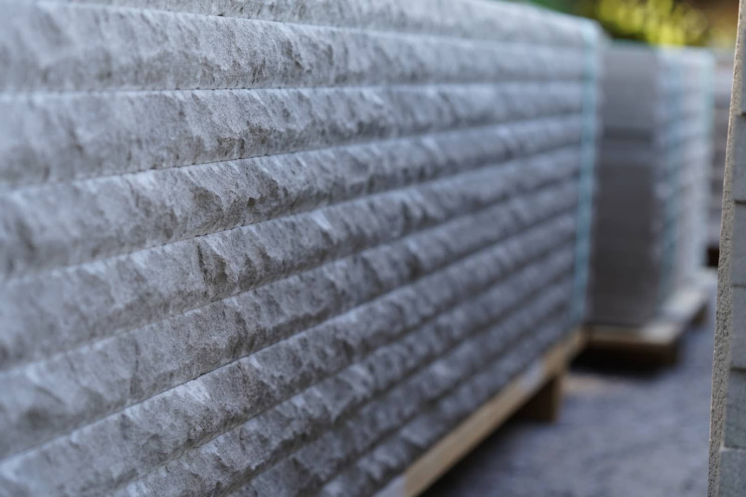 Close-up view of chiseled stone panels with a textured finish, neatly stacked on wooden pallets in an outdoor storage area.
